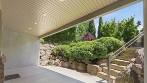 A covered outdoor area with a stone wall, greenery, and a staircase leading to an upper level. - Luxury Basement Full Apartment with Private Entrance (Provo)