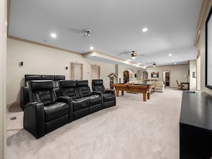 A spacious living room with a pool table, black leather recliners, and a ceiling fan.