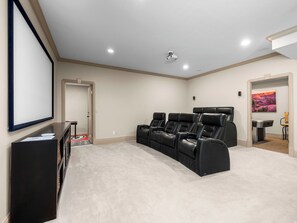 A home theater with a large screen, reclining chairs, carpeted floor, and a door leading to another room.