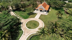An aerial view of a coastal property with a white building, a curved driveway, and a palm tree. - Dusit Thani Lubi Plantation Resort (Mabini)
