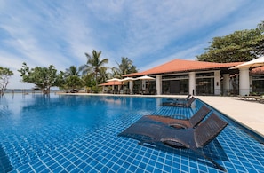 A swimming pool with lounge chairs, palm trees, and a building with a red-tiled roof.