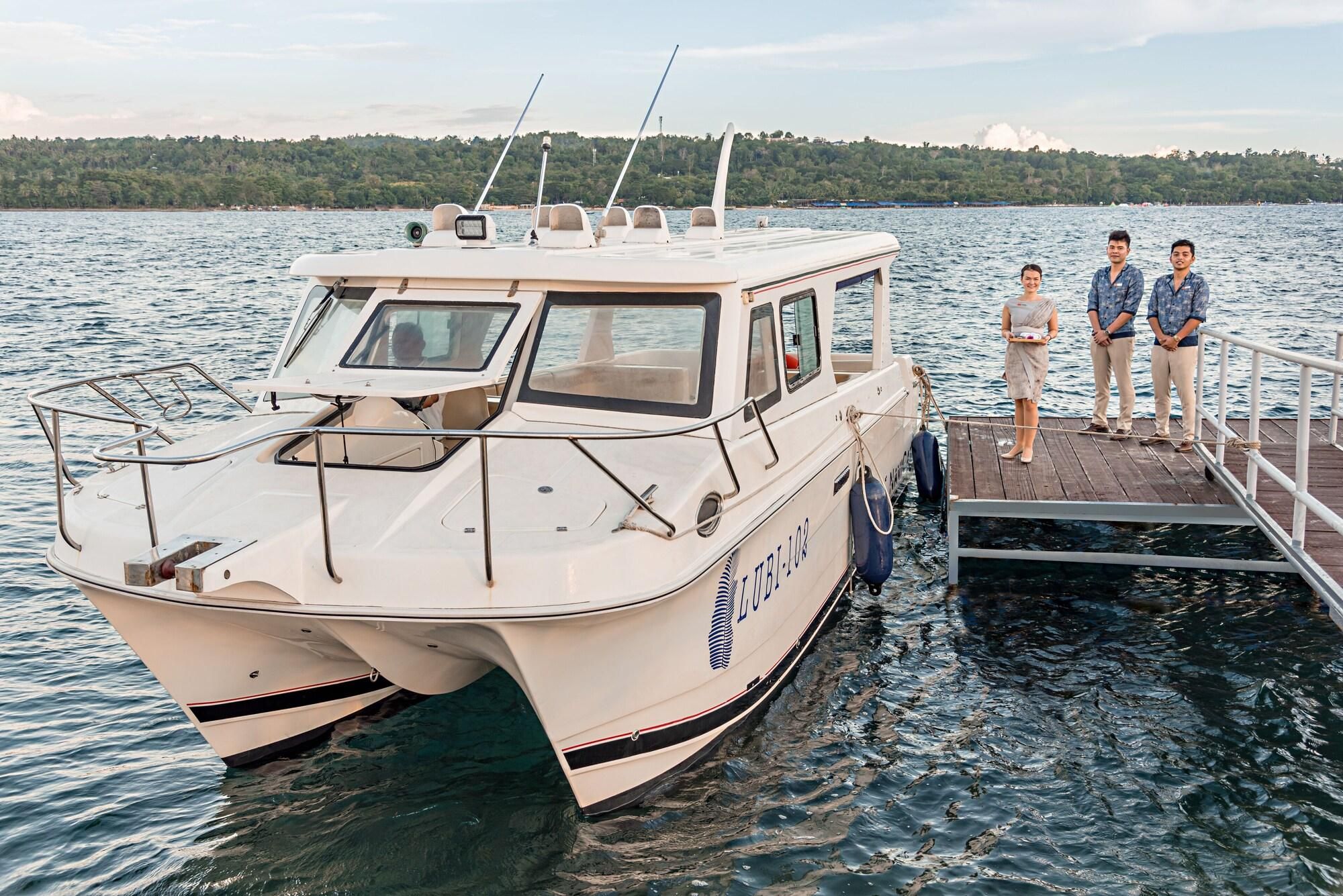 A boat docked at a pier with a forested shoreline in the background.