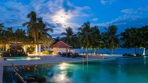 A pool area with lounge chairs and a small pavilion, surrounded by palm trees and a view of the sea. - Dusit Thani Lubi Plantation Resort (Mabini)
