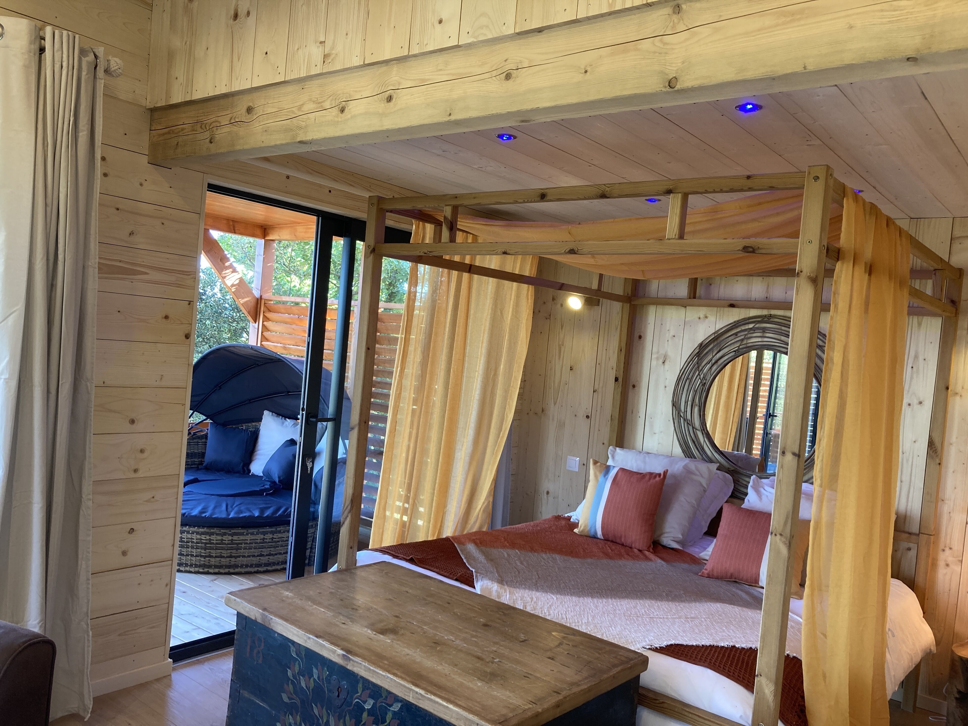 L’intérieur d’un chalet en bois, avec un lit, une table et une vue sur l’extérieur.