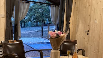Een houten terras met een tafel gedekt voor twee personen, inclusief een bloevas, een fles en een notitieboekje.