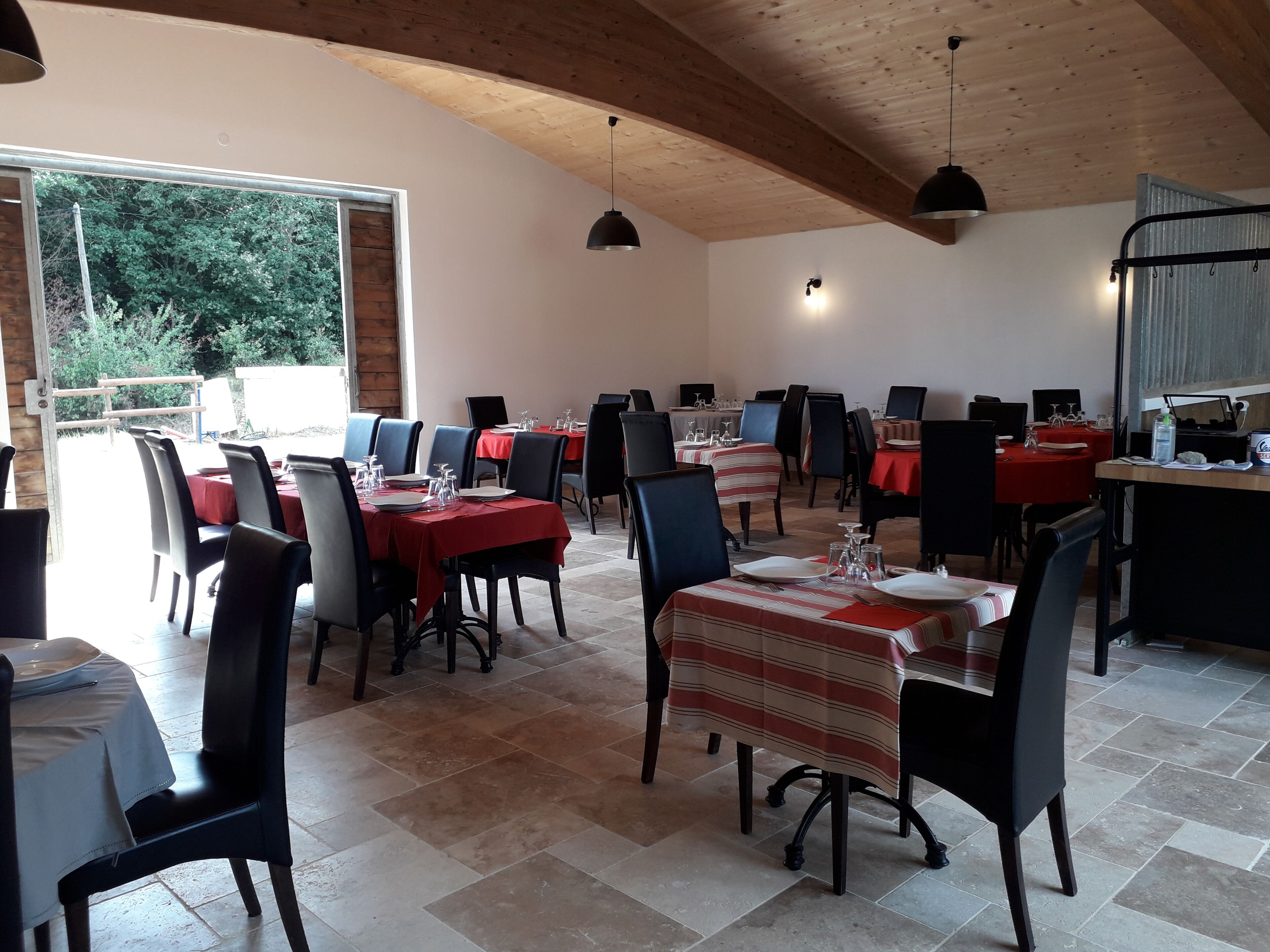 A restaurant with multiple tables, each set with plates, glasses, and cutlery. The room has a tiled floor and wooden ceiling beams.