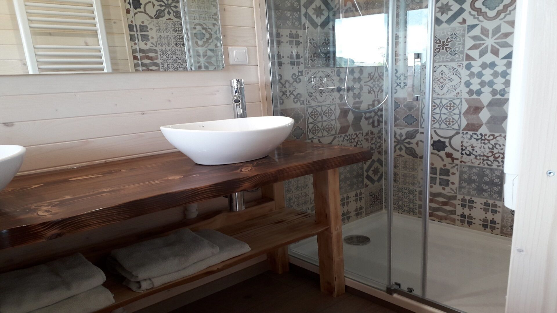 A bathroom with a wooden vanity, a white sink, and a shower with patterned tiles.