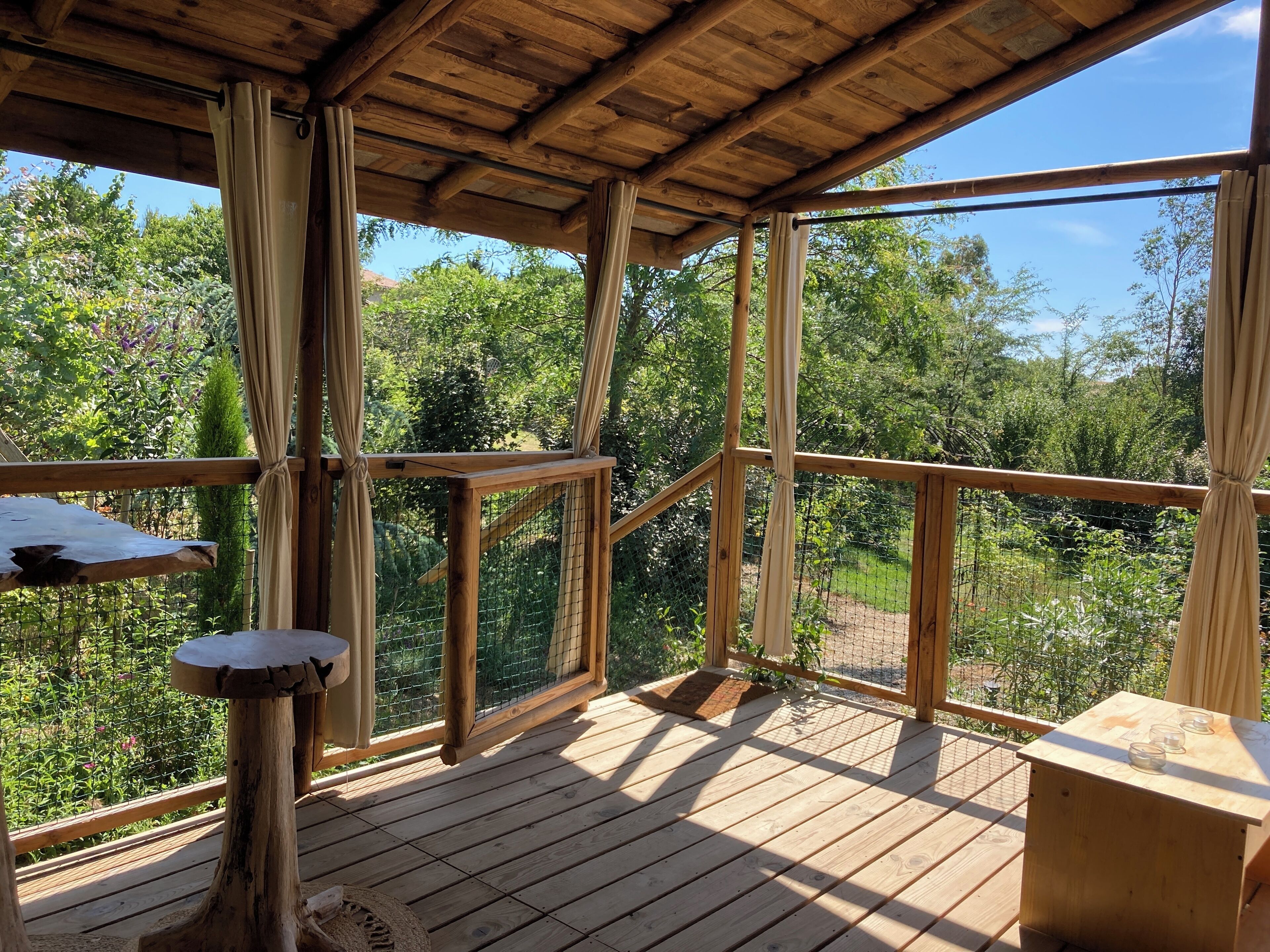 A wooden deck with a view of greenery, a wooden table, and a wooden bench.