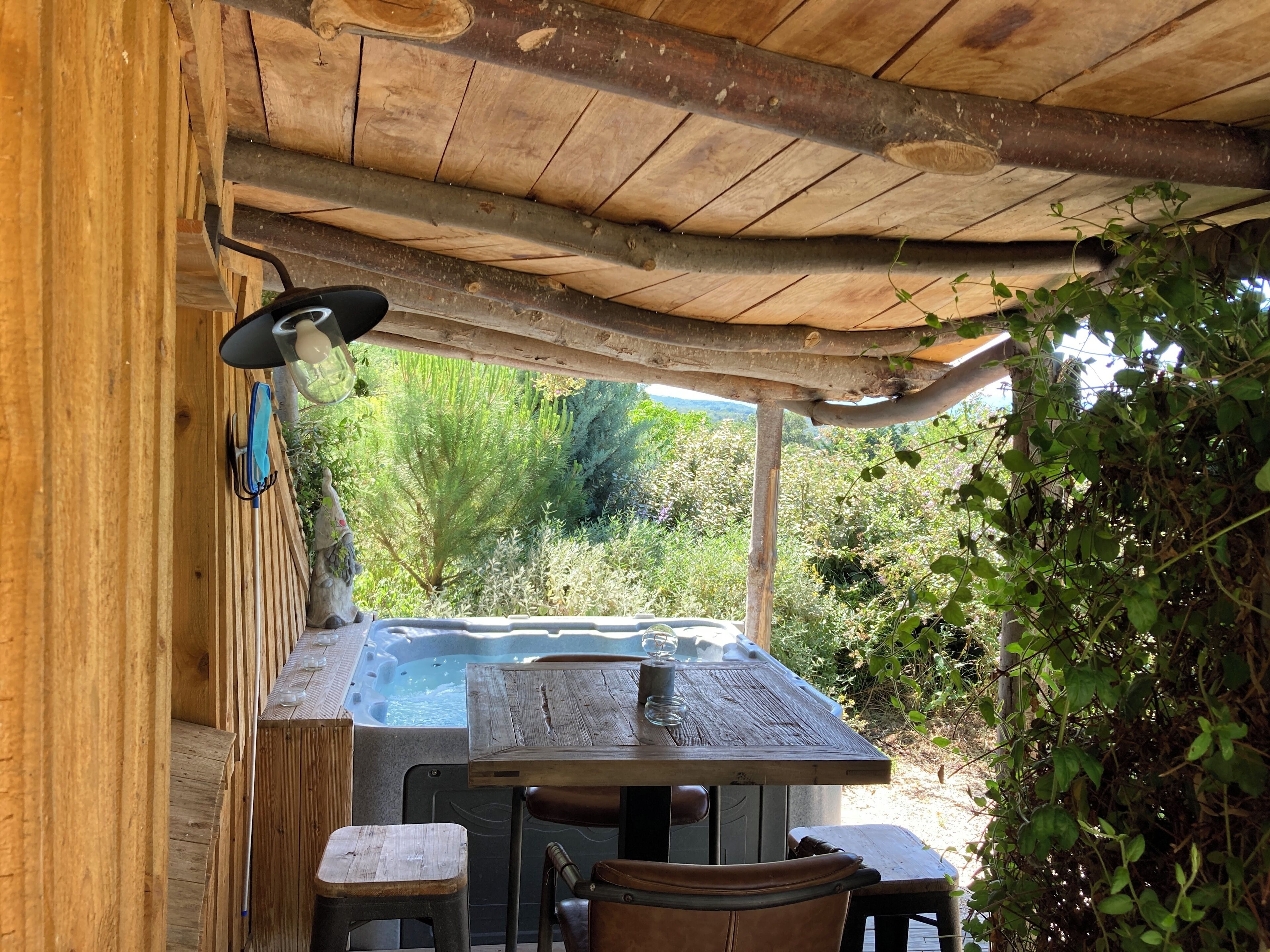 Un espacio exterior con mobiliario de madera, que incluye una bañera de hidromasaje, mesas y sillas.