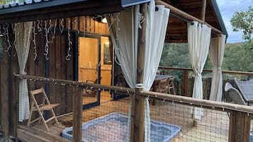 A wooden cabin with a covered deck, a small pool, and a dining area.
