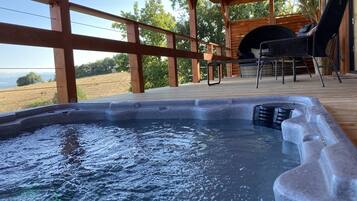 Un jacuzzi en una terraza de madera, con vista a un campo cubierto de hierba y árboles.