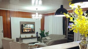 A modern living room with a wooden floor, a sofa, a TV, and a dining area. - Oasis Hotel (Palmitos)