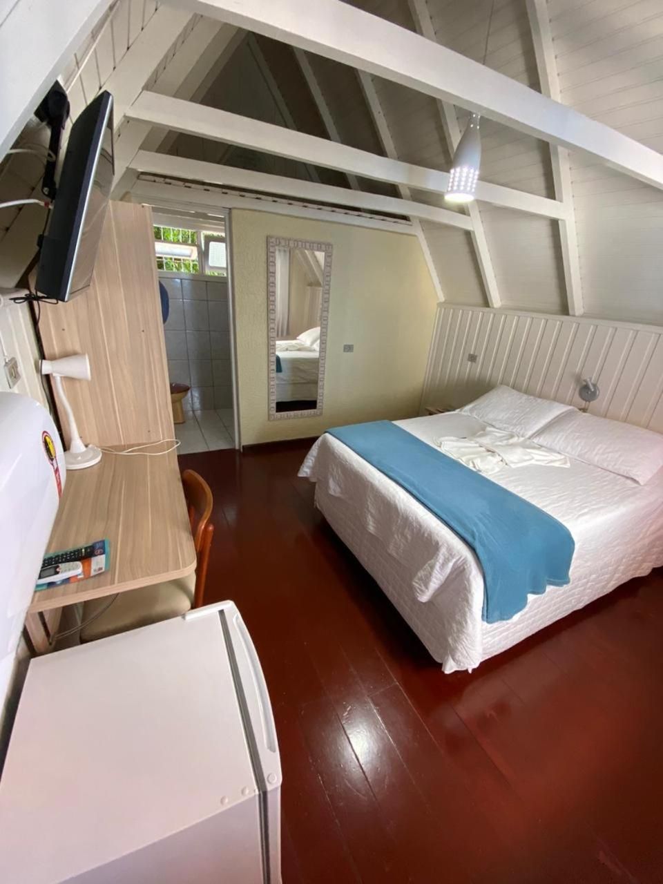 Una habitación con cama, escritorio, silla, televisor y espejo.