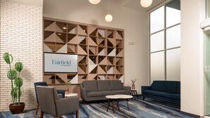 A modern hotel lobby with a brick wall, a geometric wooden panel, a gray sofa, a blue sofa, and a patterned carpet. - Fairfield by Marriott® Inn & Suites San Luis Potosi (San Luis Potosi)