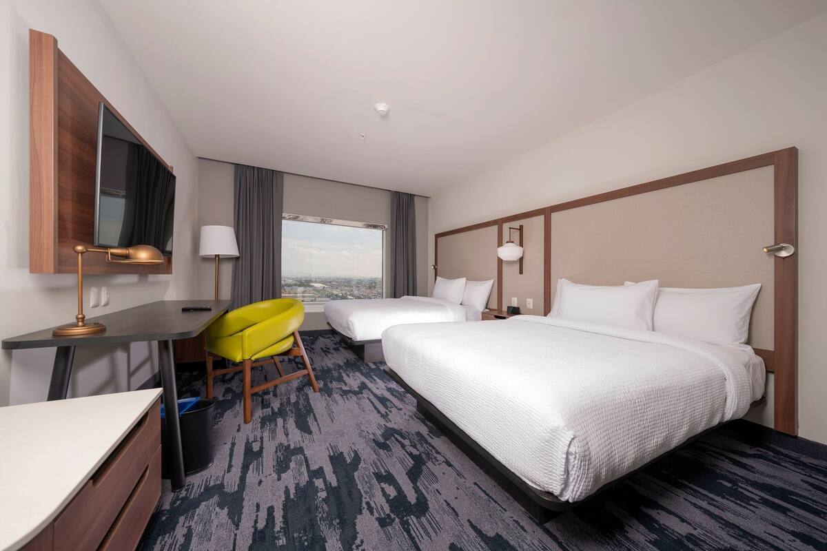 Ein Hotelzimmer mit Schreibtisch, zwei Betten, einem Sessel und einem großen Fenster.