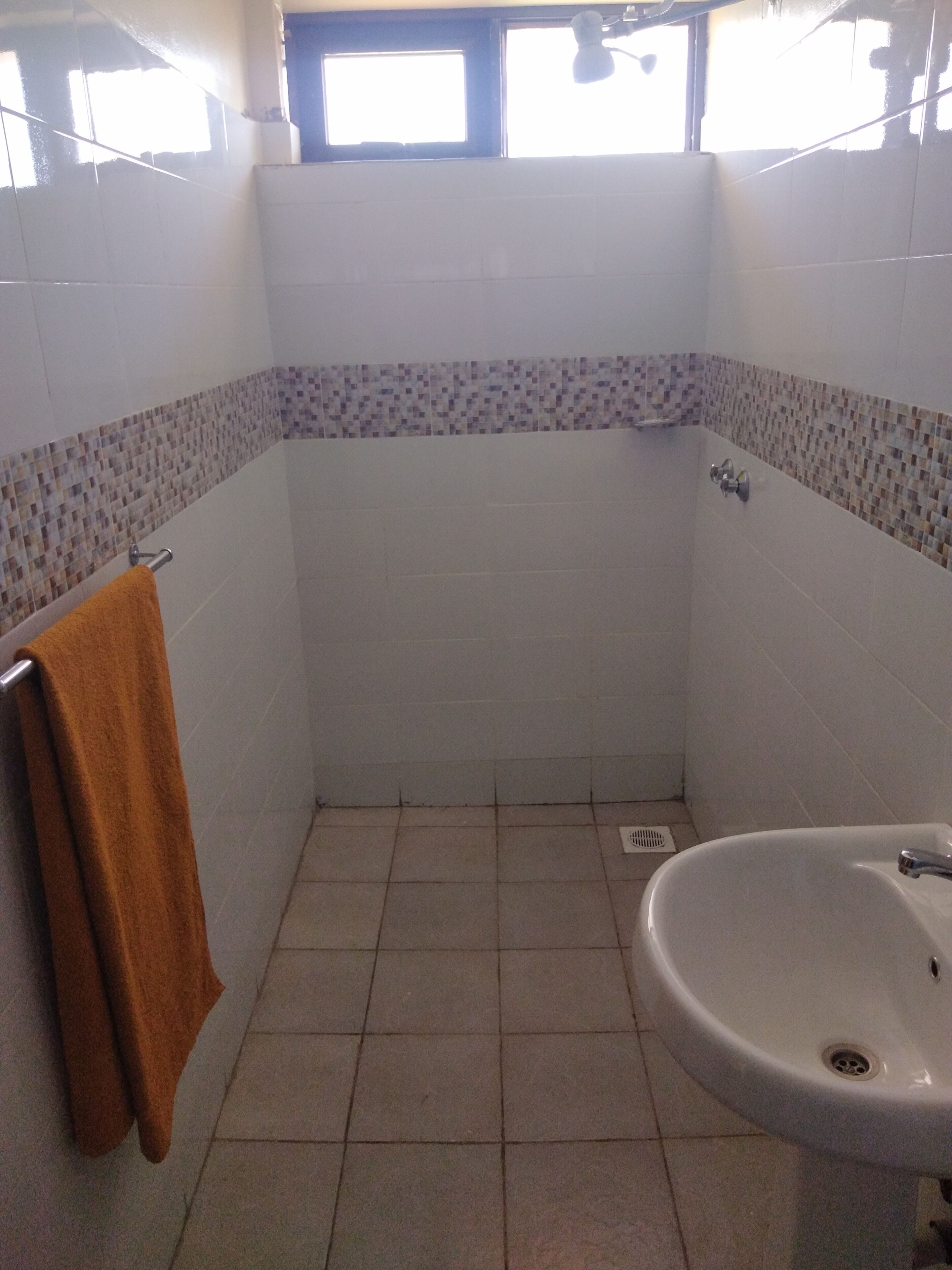Een kleine badkamer met een witte wastafel, een handdoekhouder met een handdoek, en een raam boven de wastafel.