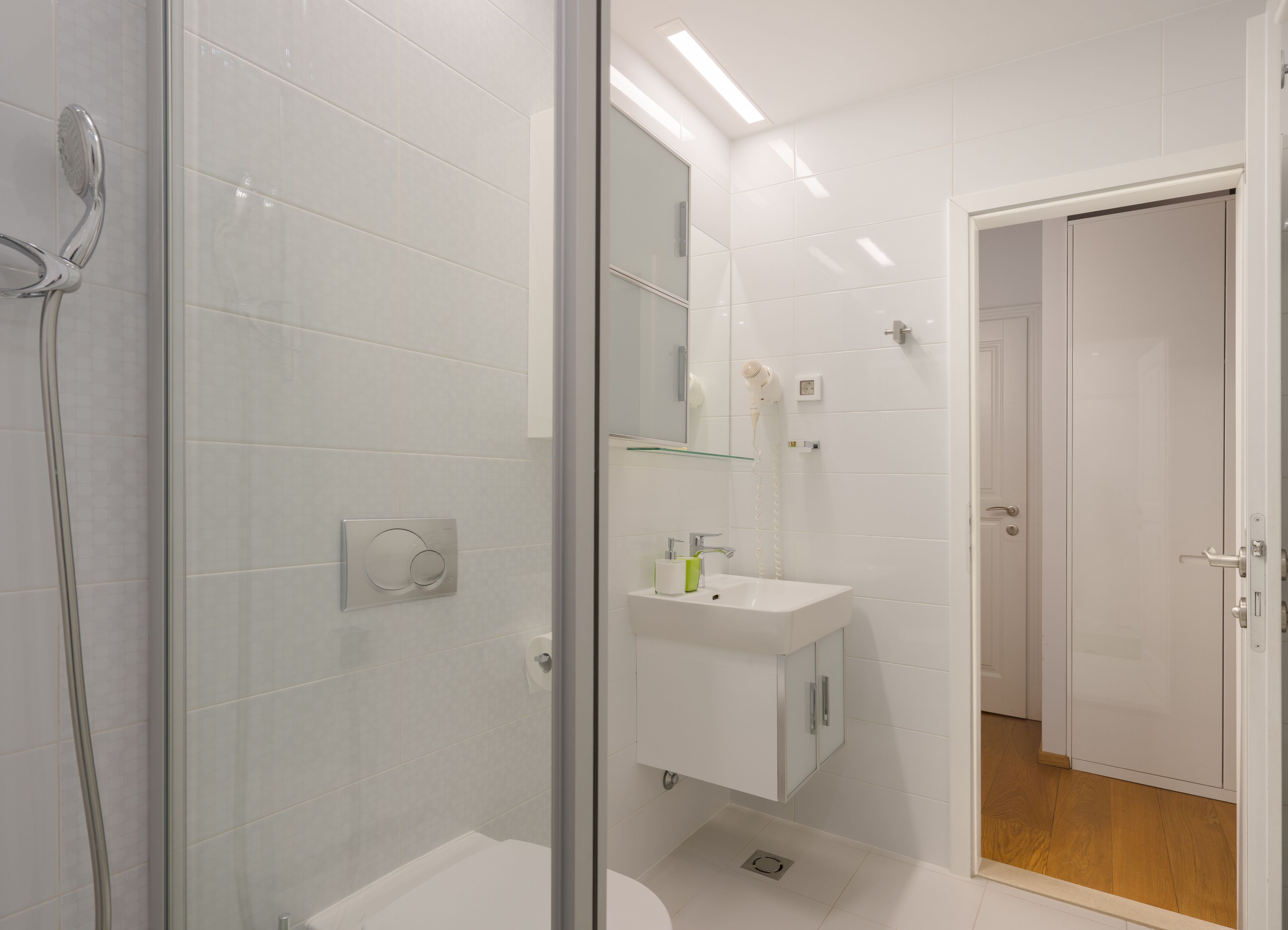 A modern bathroom with a glass shower enclosure, a white sink with a mirror above, and a door leading to another room.