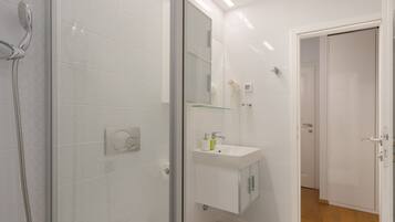 A modern bathroom with a glass shower enclosure, a white sink with a mirror above, and a door leading to another room.