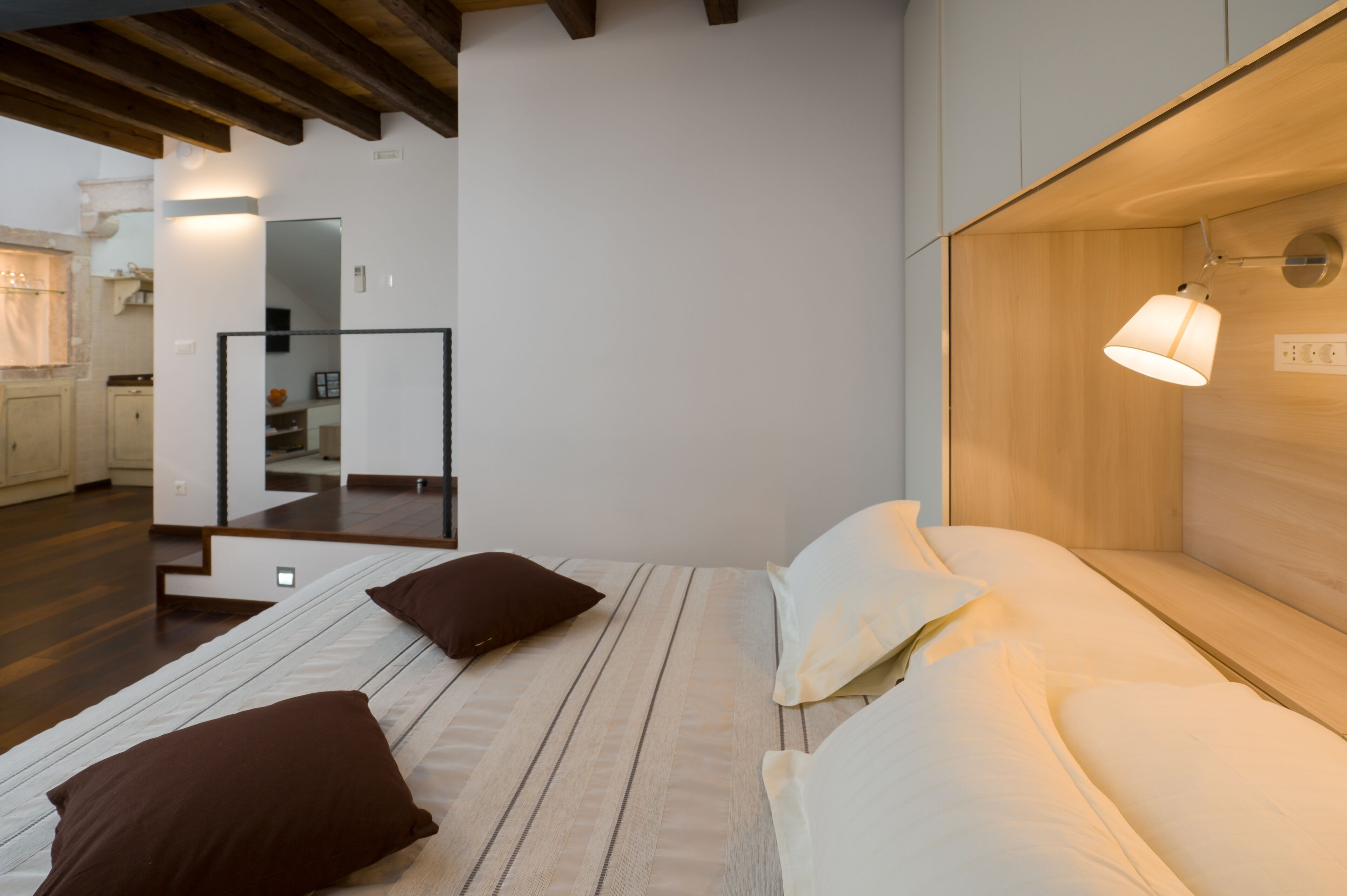 Quarto moderno com cabeceira de madeira, luminária de cabeceira e cama com travesseiros brancos e marrons.