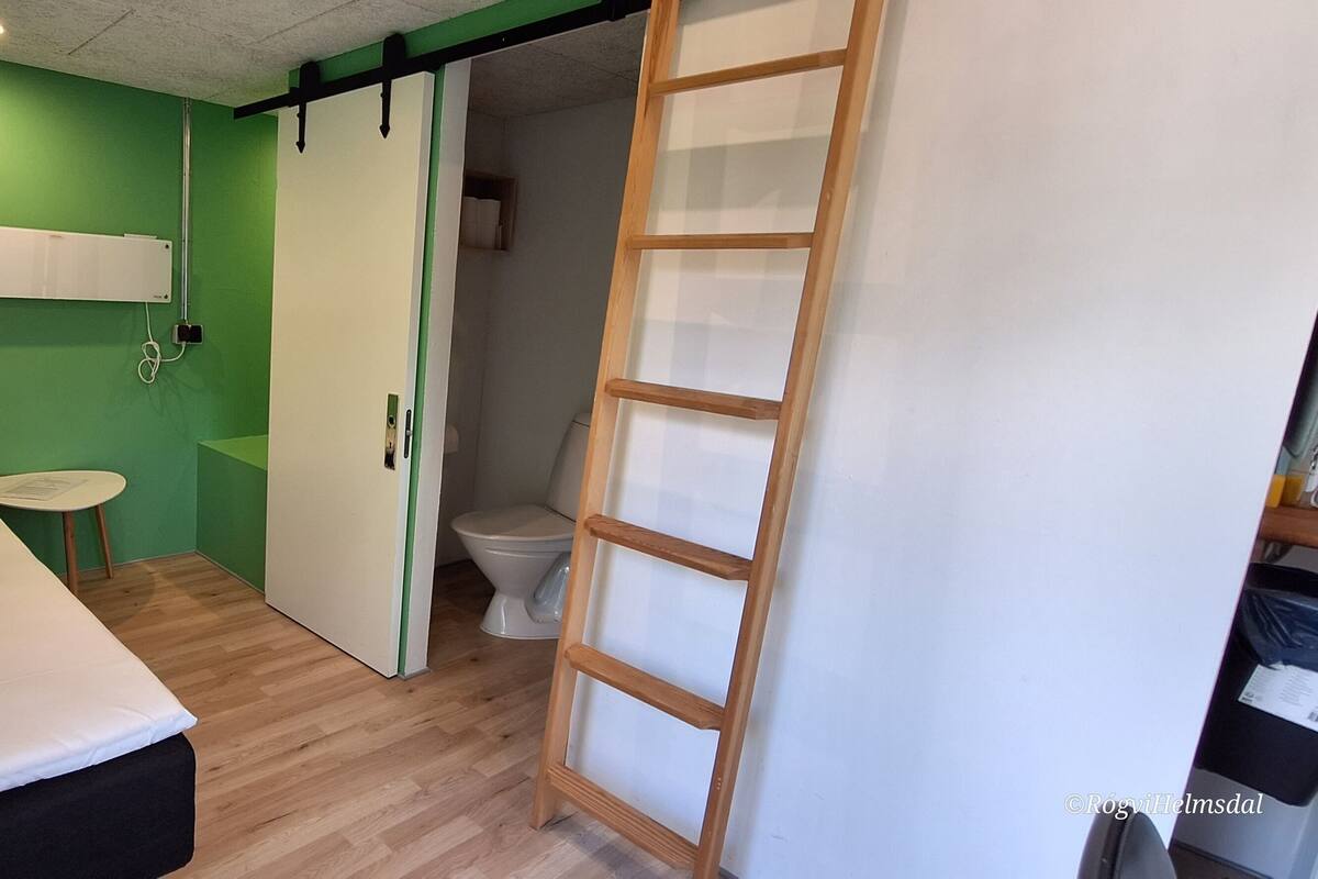 Une pièce comprenant un lit, une petite table, des toilettes et une porte coulissante donnant sur une autre pièce.