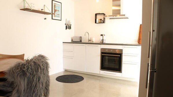 A modern kitchen with white cabinets, a built-in oven, and a toaster. There is a black rug on the floor and a dog visible in the foreground. - Tórshavn Apartment - City Center (Tórshavn)