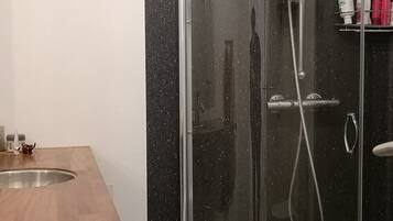 A modern bathroom with a glass shower enclosure, a wooden vanity, and a shelf with toiletries.