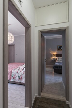 A hallway leading to a bedroom with a bed, a nightstand, and a wall-mounted lamp. - City Center Rooms (Dubrovnik)
