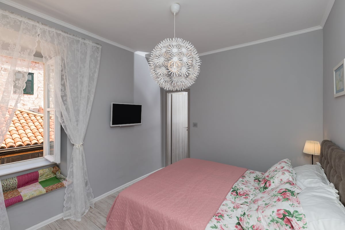 Quarto com cama, televisão, janela com cortinas e luminária decorativa no teto.