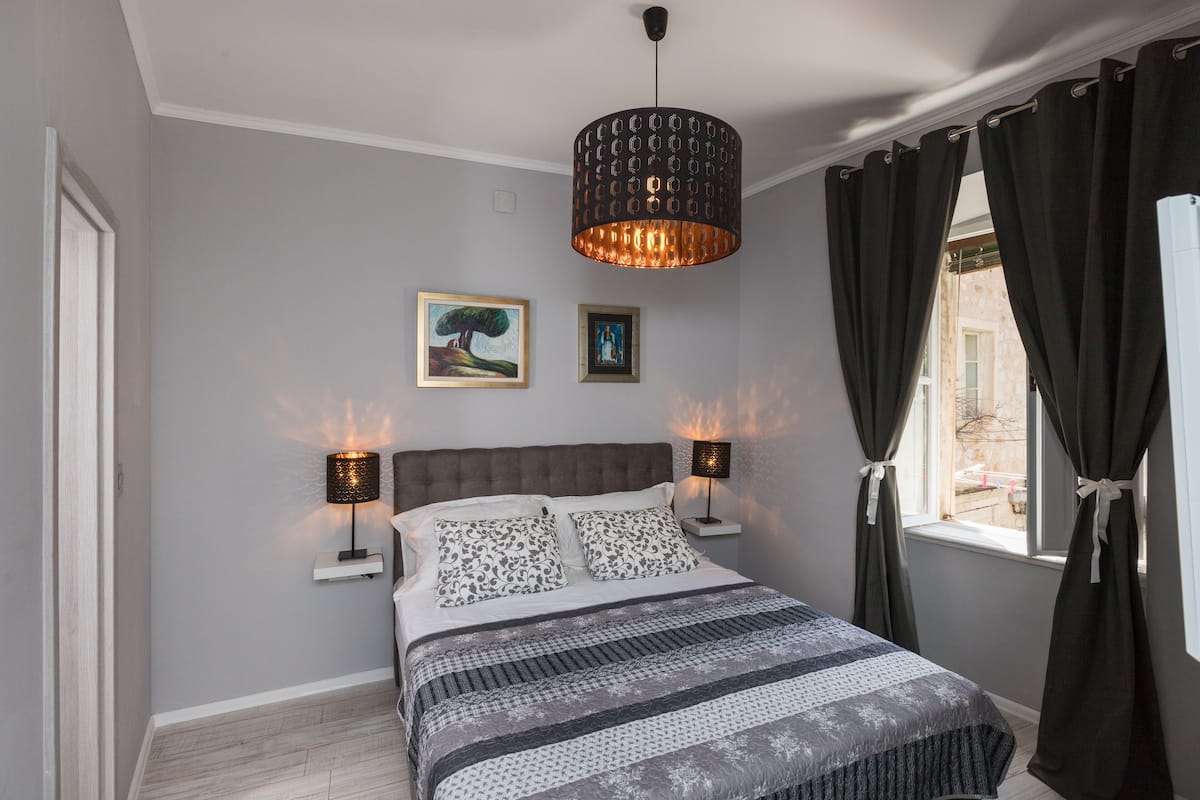 Quarto com cama, duas luminárias de cabeceira, um lustre e duas imagens emolduradas na parede.