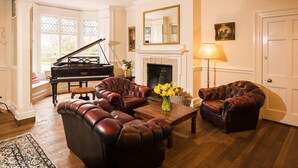 A living room with a grand piano, leather armchairs, a fireplace, and a lamp. - A beautiful home set in 11 acres of grounds, overlooking the Mendip Hills. (bristol)