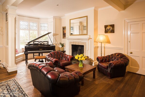 A living room with a grand piano, leather armchairs, a fireplace, and a lamp.