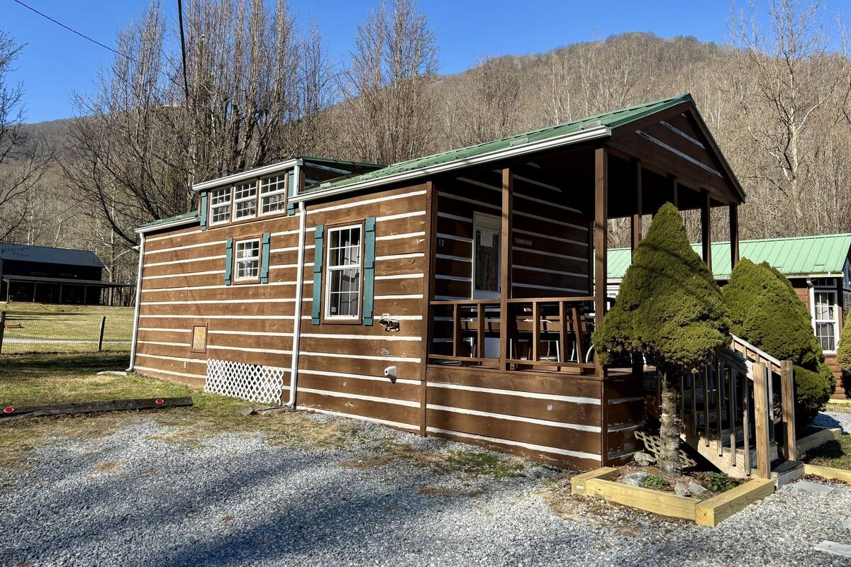 A wooden cabin with a porch, a covered deck, and a fenced yard.