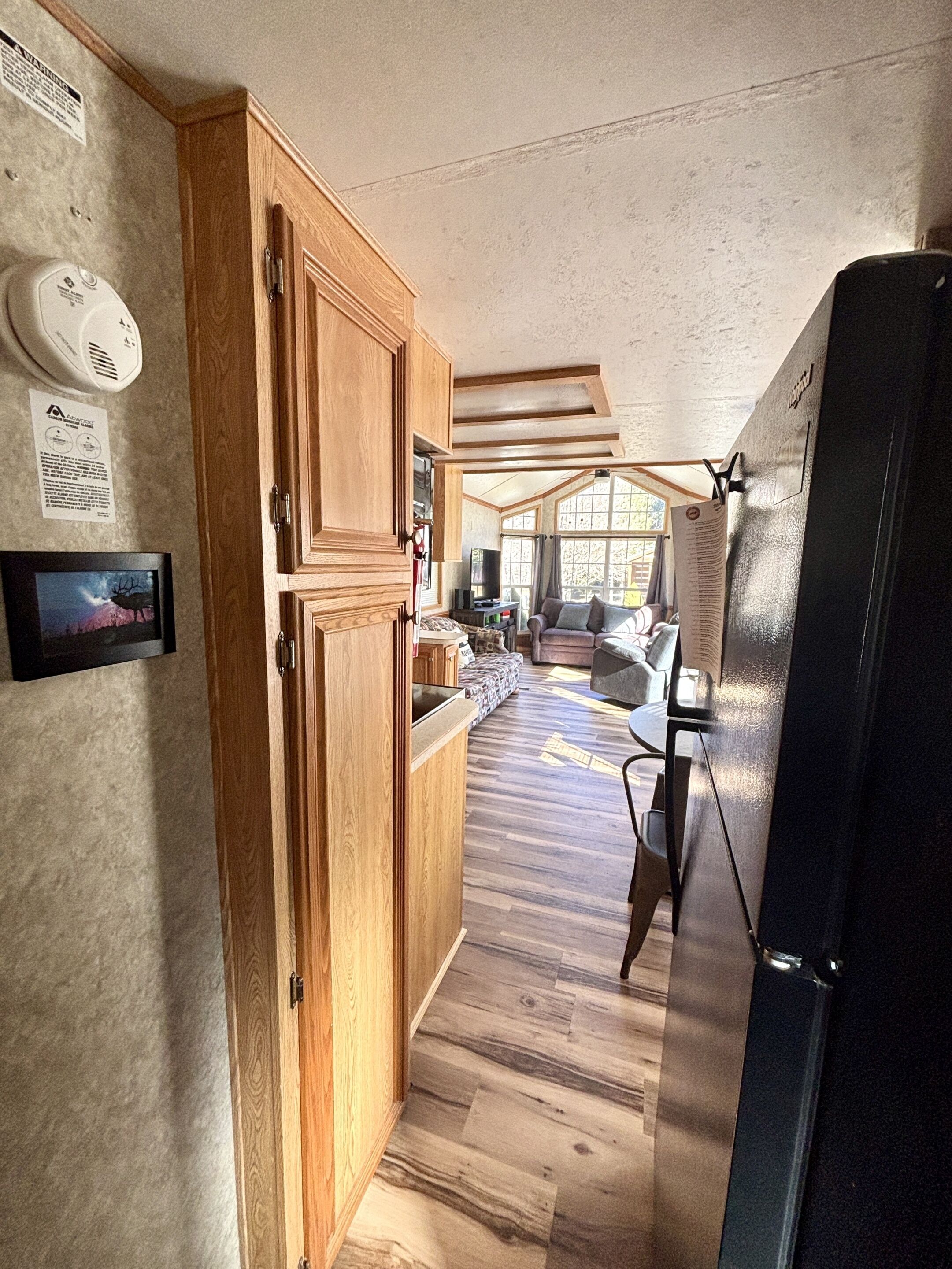 A kitchen with wooden cabinets, a black refrigerator, and a window with curtains.