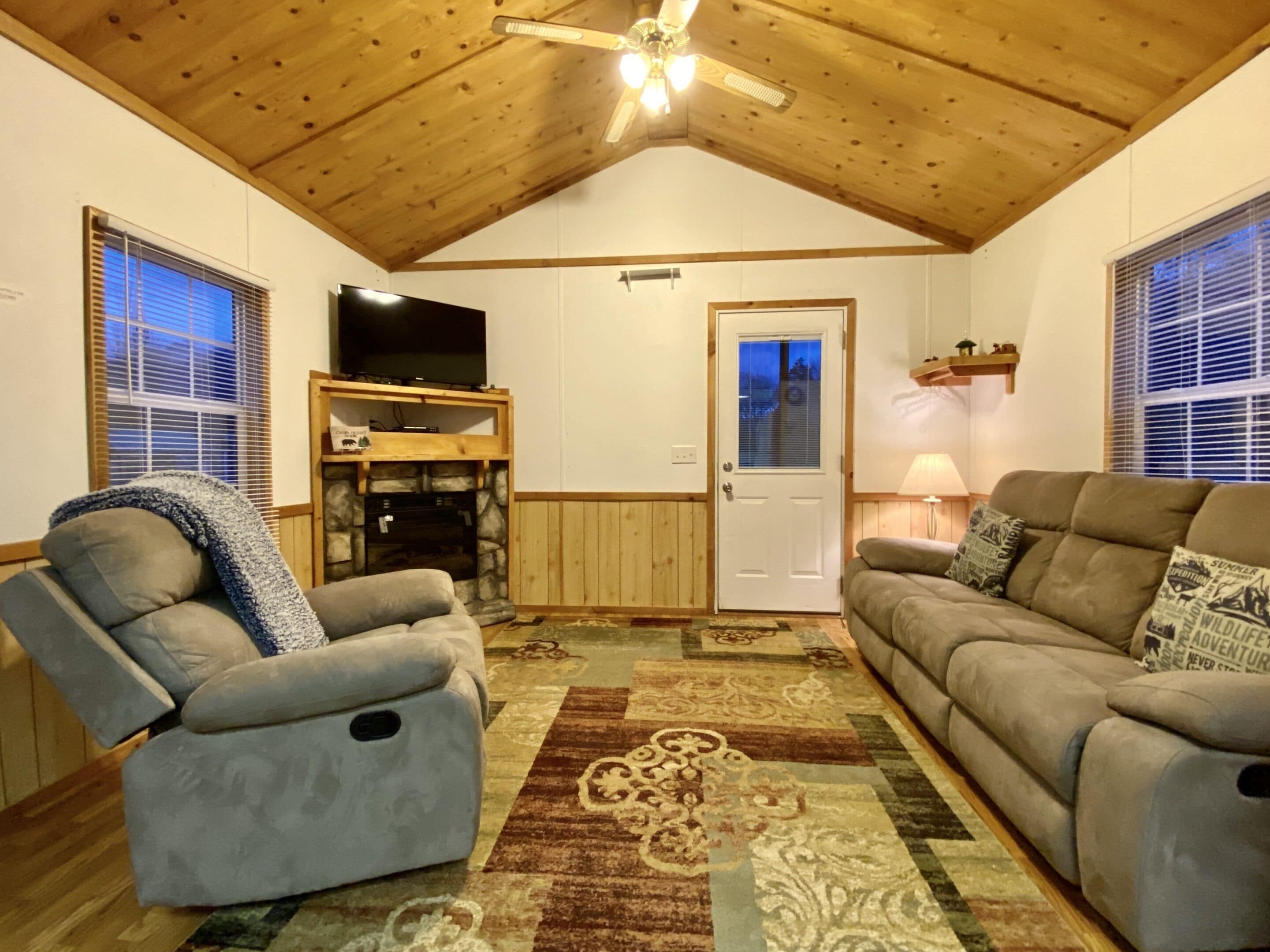 Un salon confortable avec une cheminée, un téléviseur et un ventilateur de plafond.