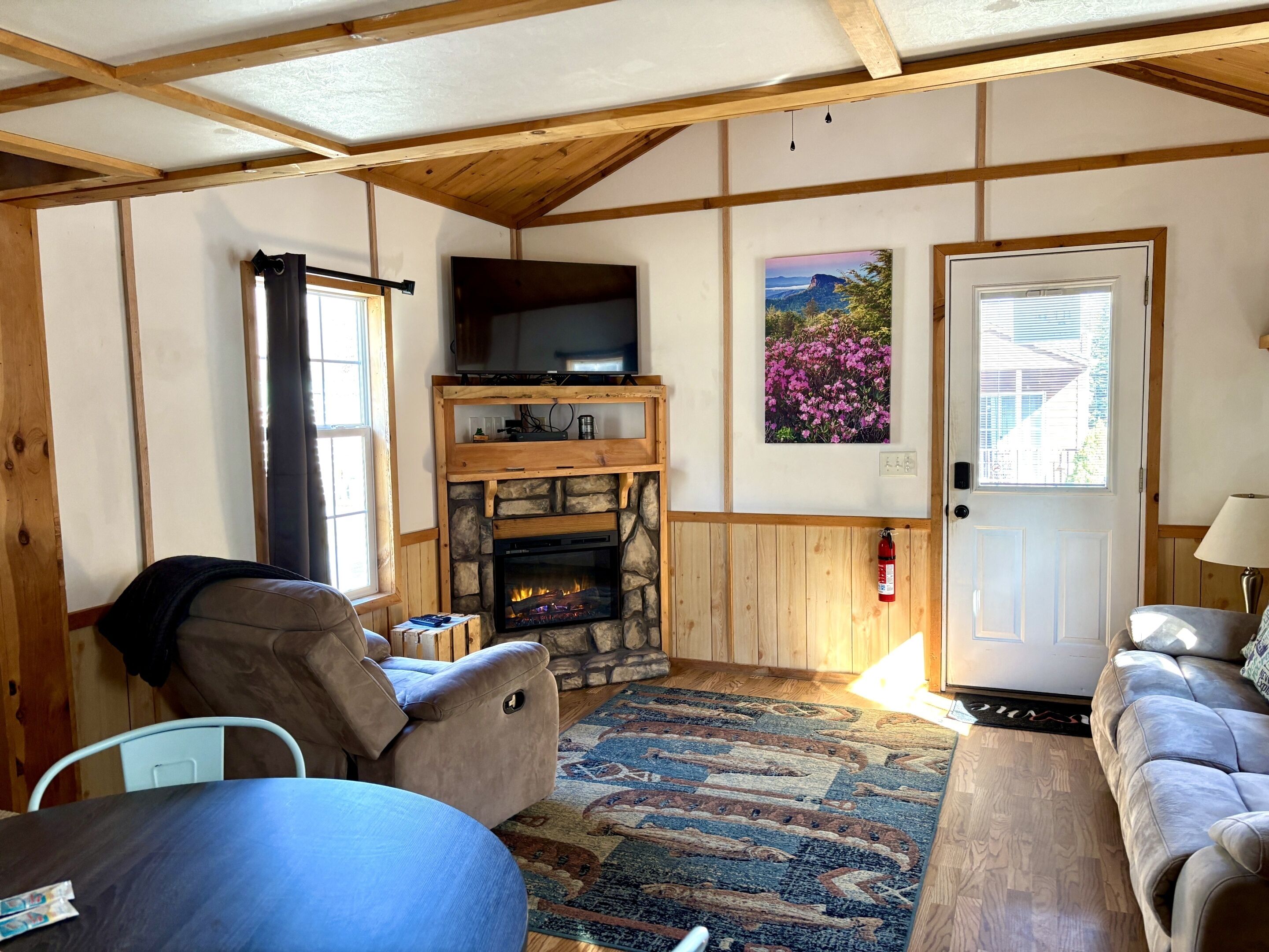 A cozy living room with a stone fireplace, a television mounted above it, and a door with a window.