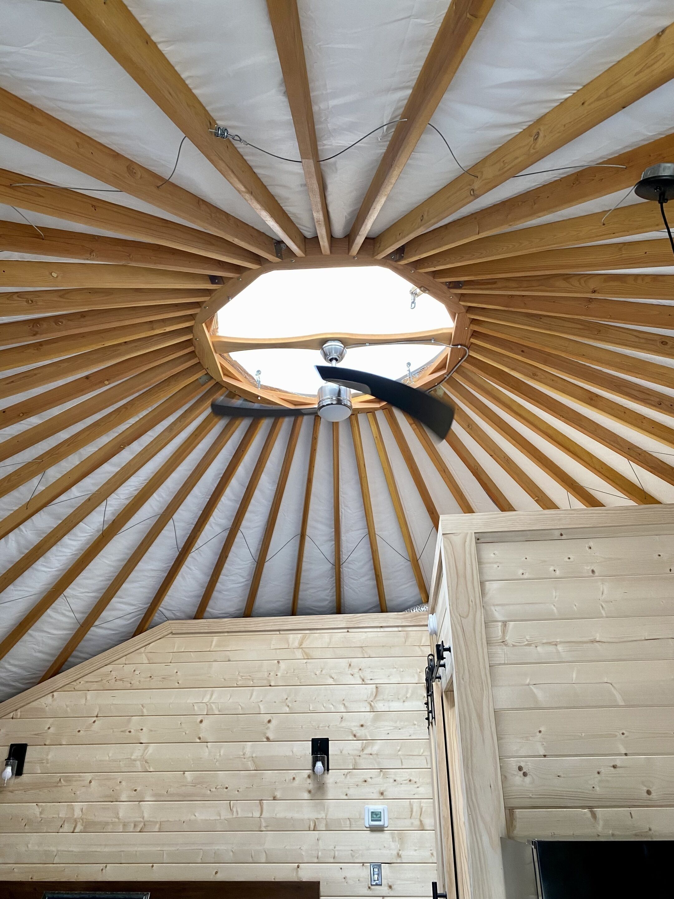 A circular wooden ceiling structure with a central fan, wooden beams, and a skylight.