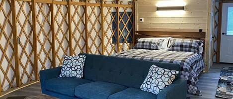 Een gezellige, goed verlichte tentkamer met een bed, een slaapbank en een klein tafeltje.