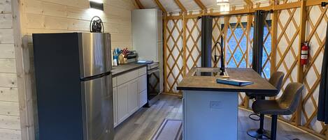 Eine kleine Küche mit Kühlschrank, Herd und Spüle, Holzwänden und einer kleinen Essecke mit Barhocker.