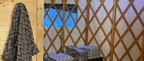 Una habitación con techo inclinado, panel de celosías de madera, una cama con colchón azul, un aparador de madera oscura con cajones y una colcha estampada colgada en la pared.