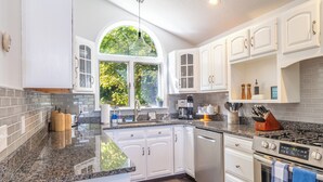 A kitchen with white cabinets, granite countertops, a large window, and a gas stove. - Lakeshore Cottage- Family and Pet Friendly, Lakefront, Fireplace, and Gameroom (Fort Ann)