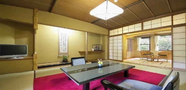 Ein traditioneller japanischer Raum mit Tatami-Bodenbelag, einem niedrigen Tisch mit Kissen und Schiebetüren.