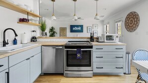 A modern kitchen with stainless steel appliances, wooden shelves, and a blue towel hanging on the oven. - Only 5 blocks to King! | Rose and Petunia Suites (Charleston)