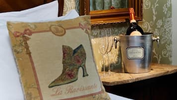 A pillow with a boot design and the text "La Ravissante" on a bed. A metal bucket with a bottle of champagne and glasses is on a wooden table.