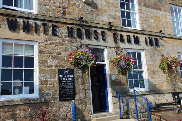 The exterior of the White Horse Farm Inn, featuring stone walls, a welcoming sign, and flower baskets. - White Horse Farm Inn (Pickering)