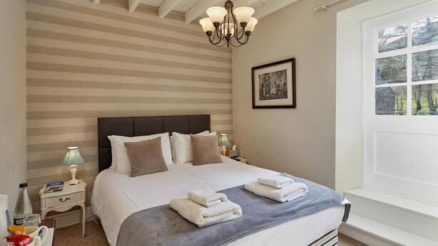 Une chambre à coucher bien rangée, avec un grand lit, une lampe de chevet et une fenêtre donnant sur un beau paysage.
