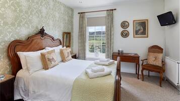 Quarto com cama grande, escrivaninha, cadeira, televisão e janela com cortinas.