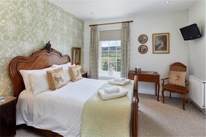 A bedroom with a large bed, a desk, a chair, a television, and a window with curtains. - White Horse Farm Inn (Pickering)