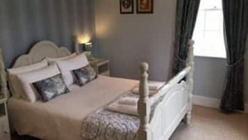 A bedroom with a four-poster bed, a nightstand, a bedside table, and two framed pictures on the wall.