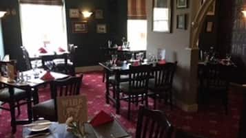 Un comedor con mesas dispuestas para el servicio, cuadros en las paredes y una alfombra roja.