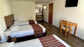 A hotel room with two beds, a wooden desk, and a television on the wall.